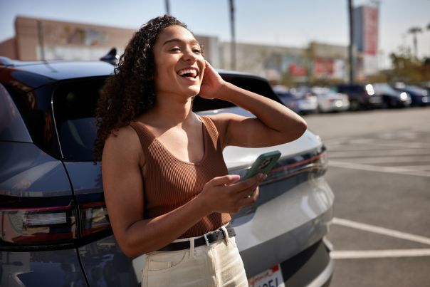 A person casually leans on their electric vehicle while holding their phone and smiling.
